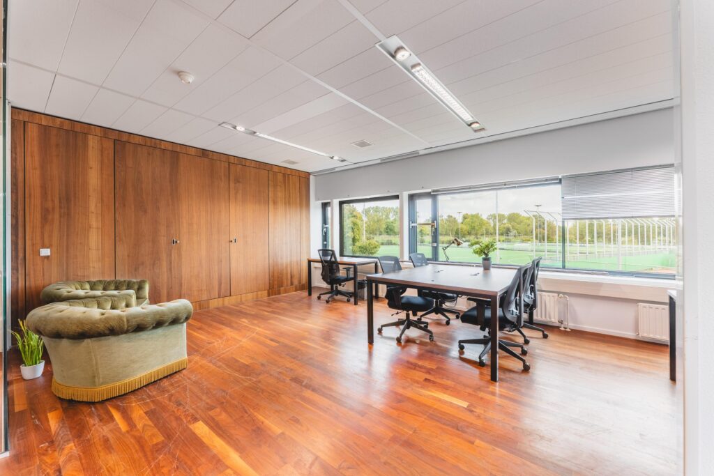 Ruim en licht kantoor met houten vloer, bureau-opstelling, en uitzicht op sportvelden aan de Prof. W.H. Keesomlaan.